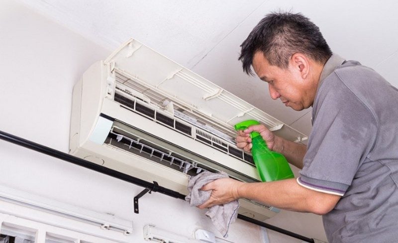 A person cleaning a air conditionerDescription automatically generated